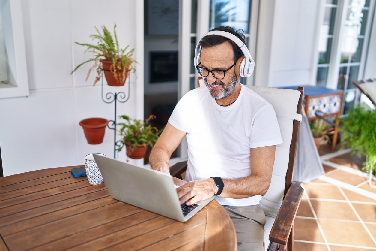 Mann mittleren Alters mit Laptop und Kopfhörern auf workation
