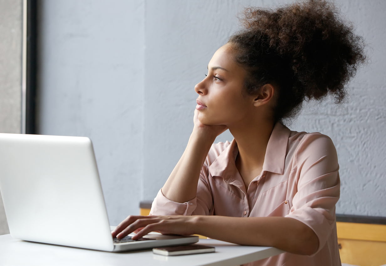 junge Frau vor laptop schaut nachdenklich aus dem fenster